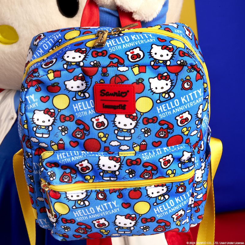 Hello Kitty holding the Loungefly Sanrio Hello Kitty 50th Anniversary All-Over Print Nylon Mini Backpack to the camera 